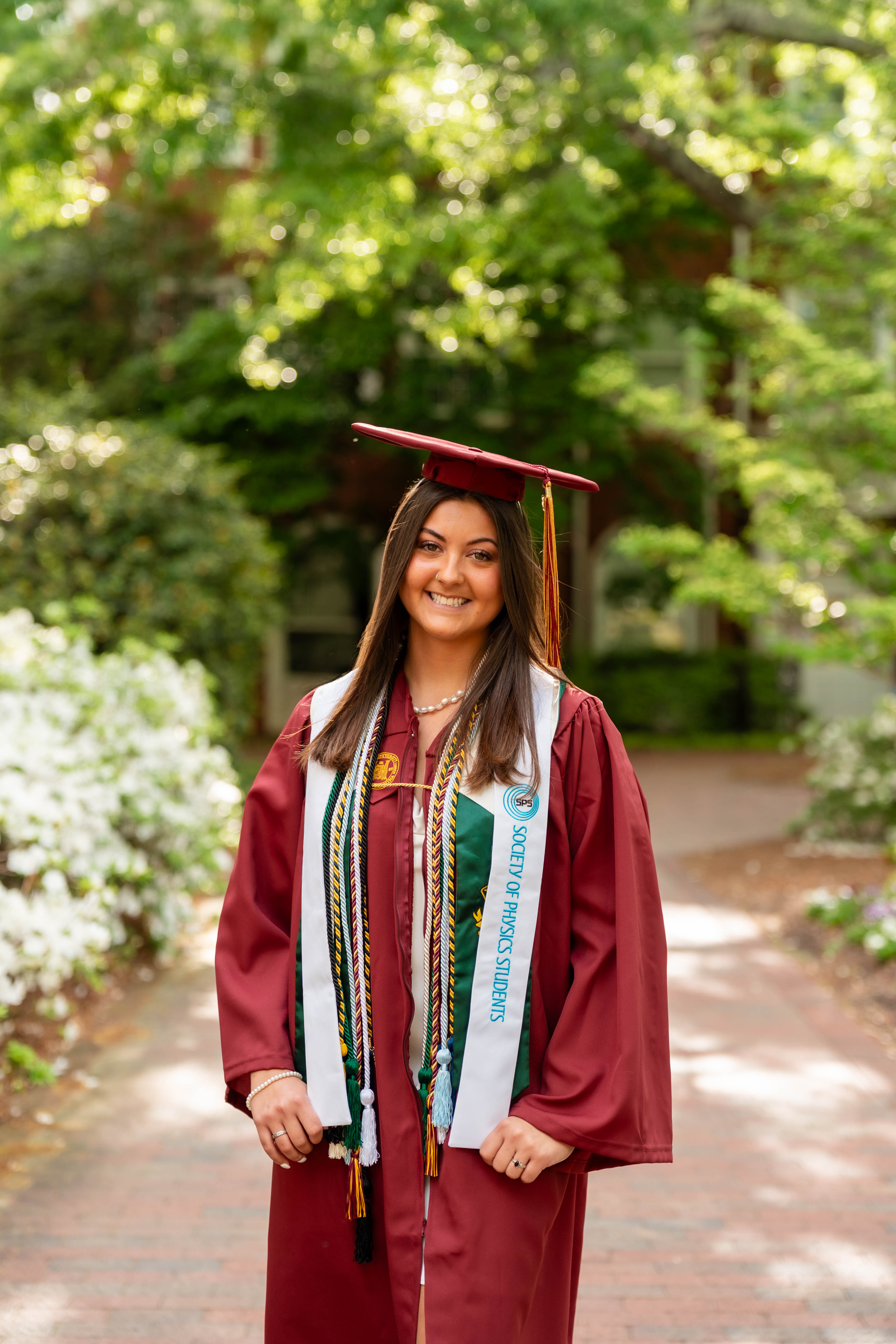 A young woman stands in a maroon cap and gown