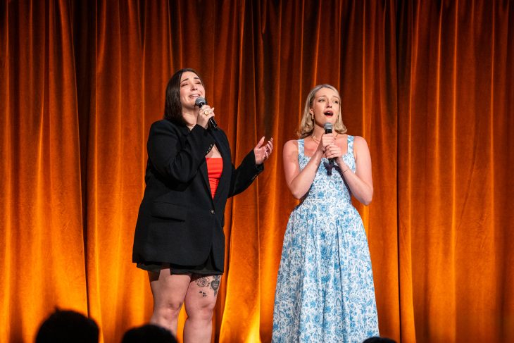 Two people sing on a stage with microphones