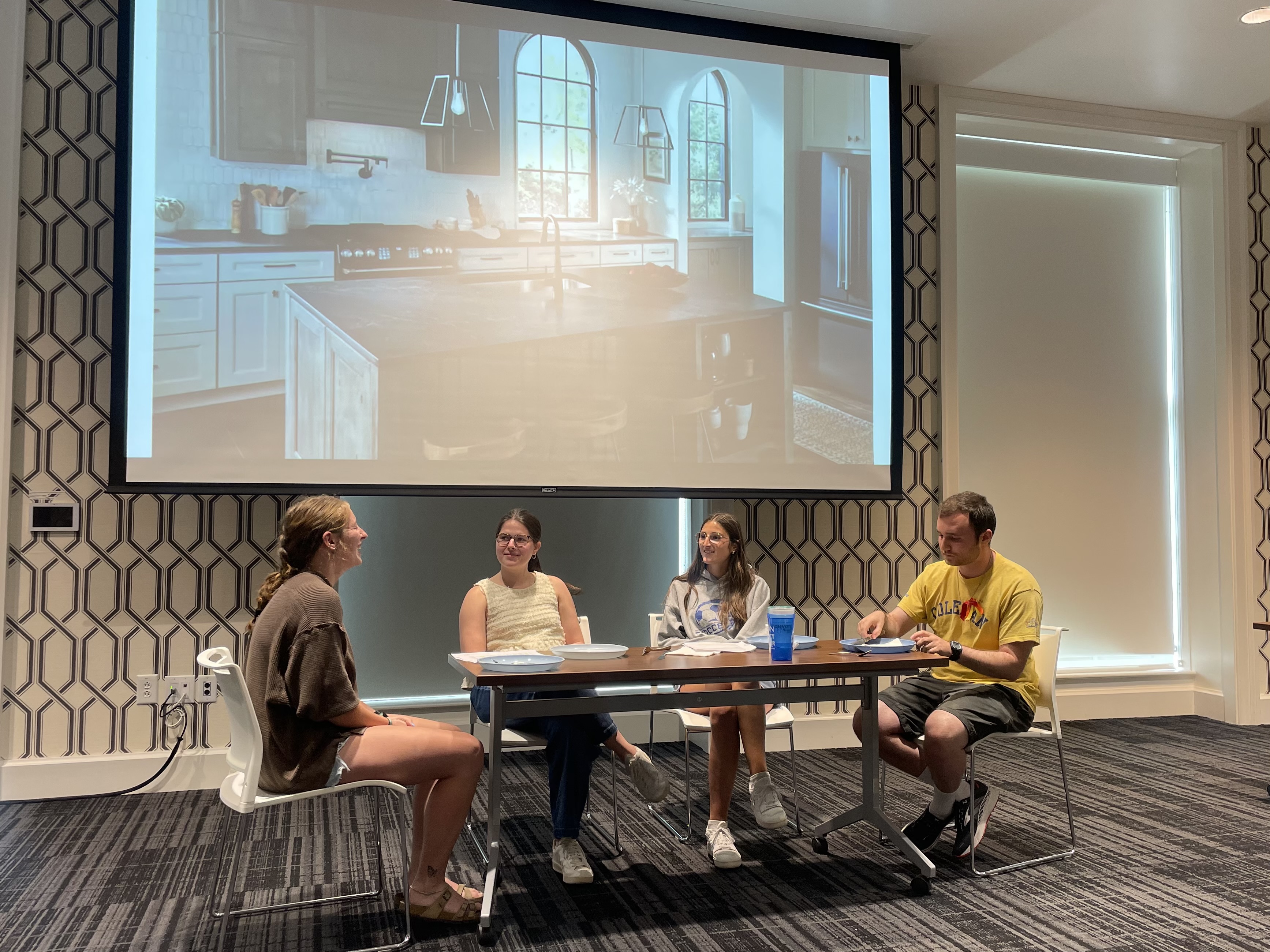 This photo shows four students seated around a table performing a family kitchen scene, likely improvising or re-interpreting a moment from Una familia perfecta during a class activity or theatrical exercise.