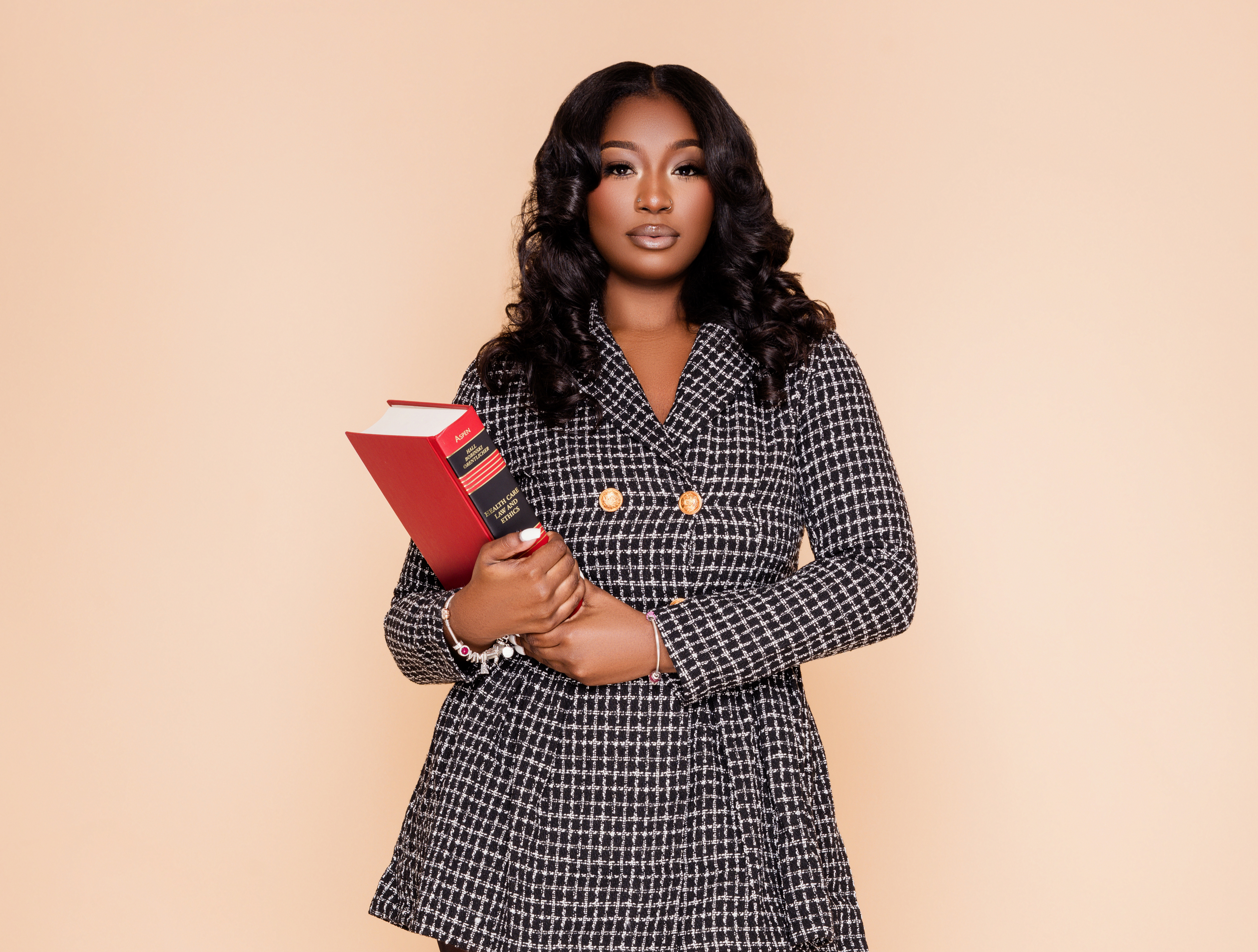 A woman posed for a photo wearing a black and gray dress, holding a health law book. She has a serious look on her face.