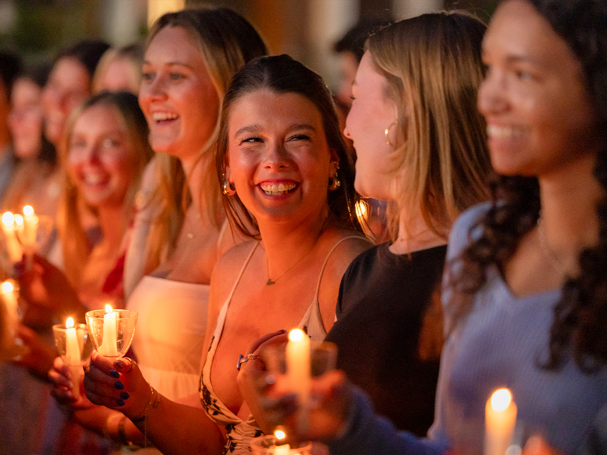 A group of smiling seniors hold glowing candles during the Numen Lumen ceremony at Elon University.