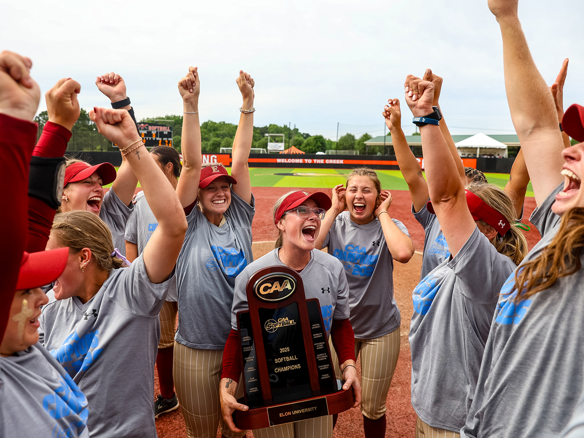 The Elon University softball team celebrates on the field with raised arms and joyful expressions after winning the 2025 CAA Championship.
