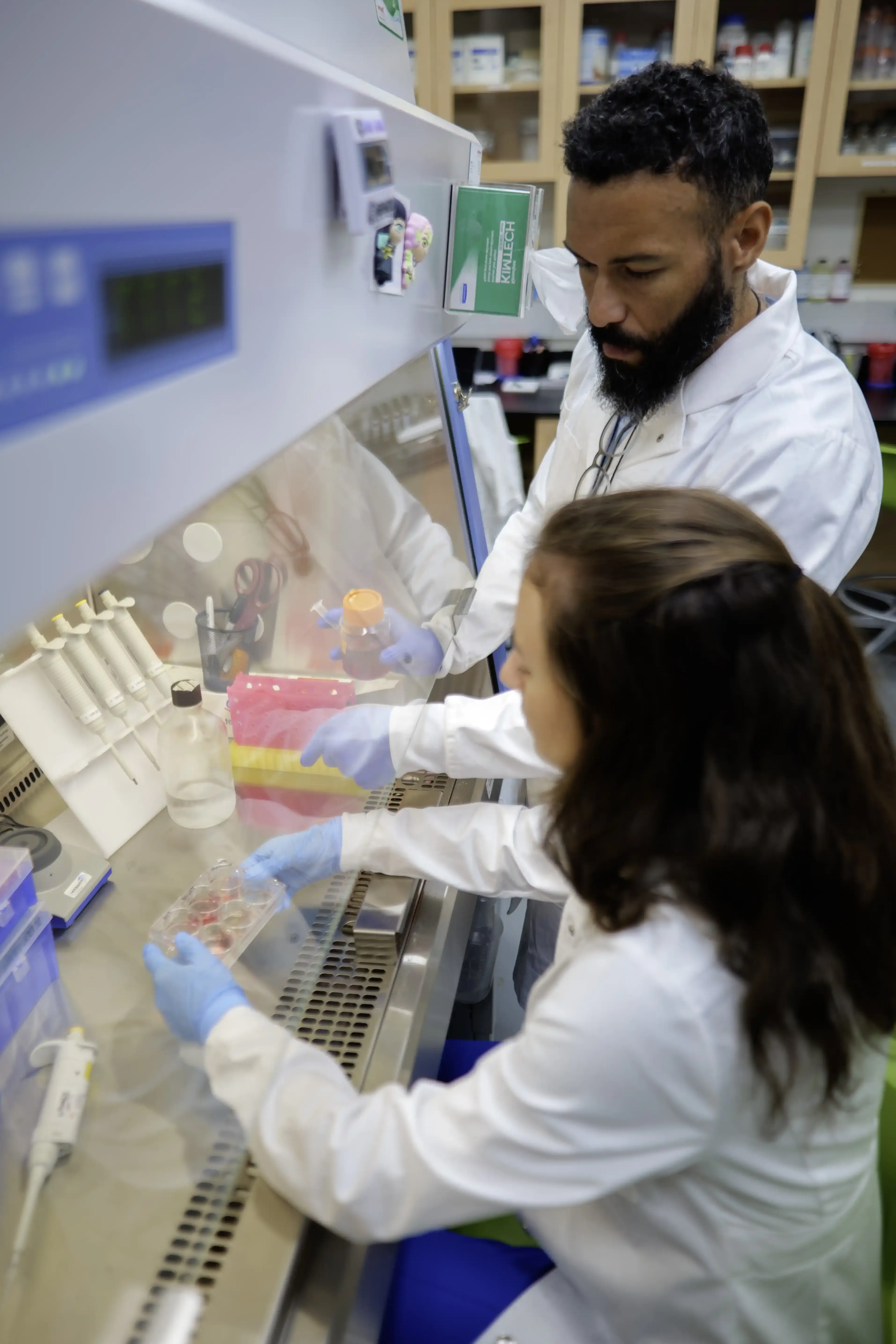 Two people work together in a lab setting with white lab coats on