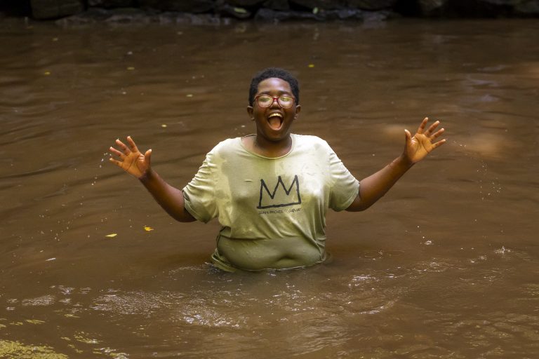 A young boy stands in water waste deep smiling with his hands outstretched
