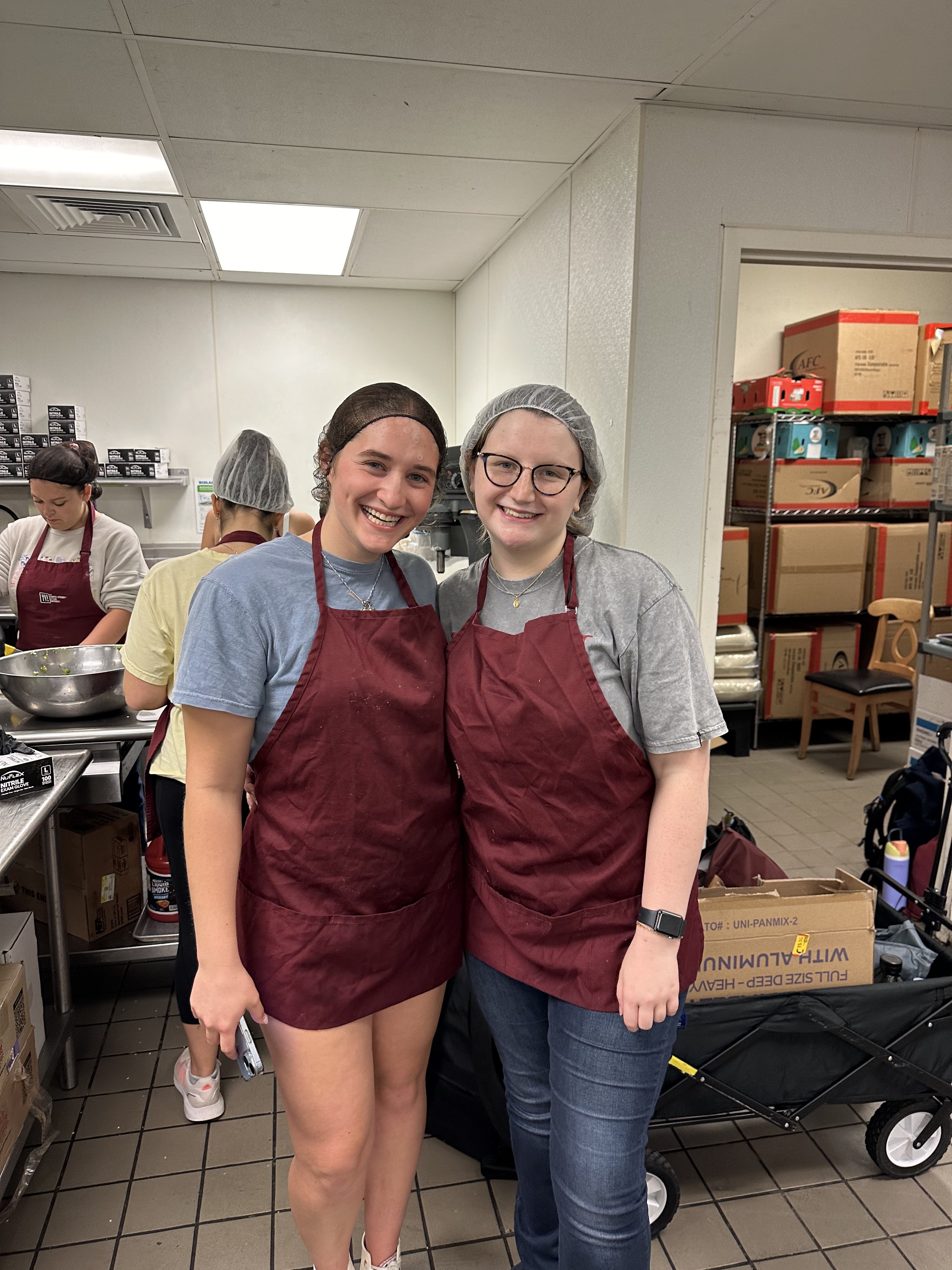 Two people in maroon aprons pose for a photo smiling