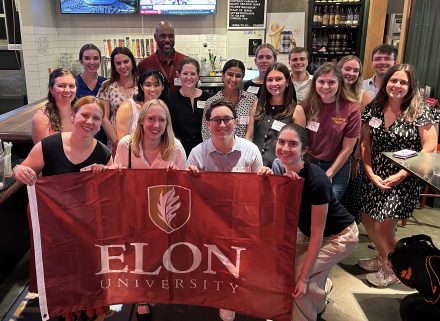 A group of people hold a maroon banner with the Elon name and logo