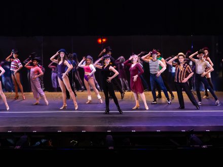 A line of actors singing and dancing onstage