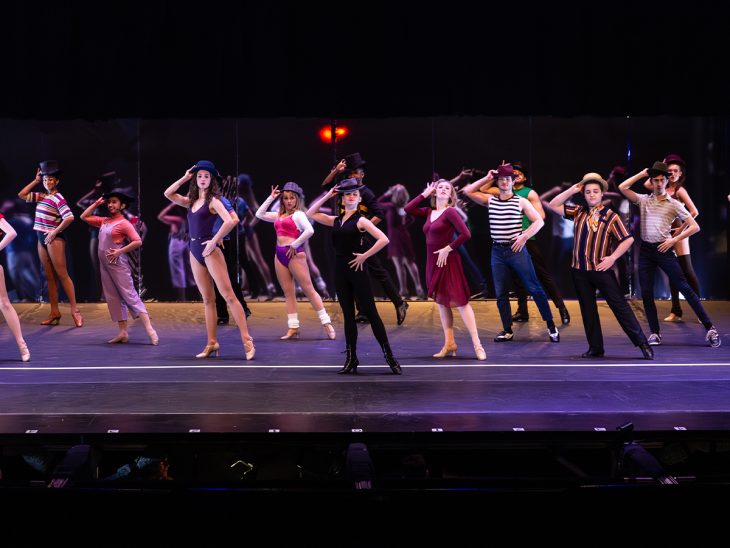A line of actors singing and dancing onstage