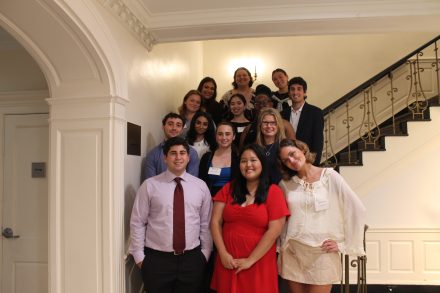 A group of professionally dressed young adults pose together on a staircase, smiling for a group photo at a formal event.