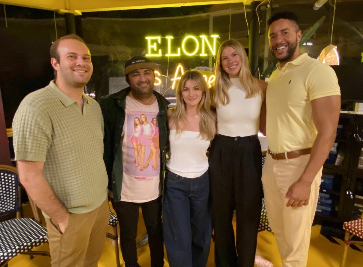 Five attendees pose for a group photo in front of a neon “Elon Los Angeles” sign.