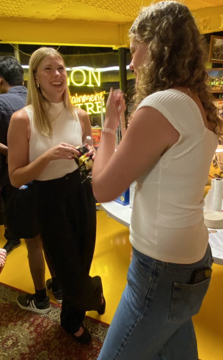 Two women laugh and chat near a refreshment table during the Elon event.