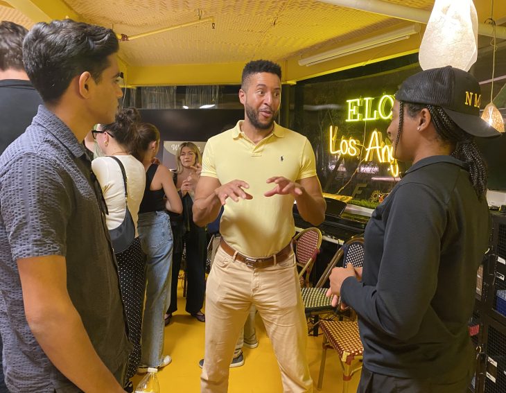 A man animatedly speaks with two other attendees at an Elon alumni event in Los Angeles.