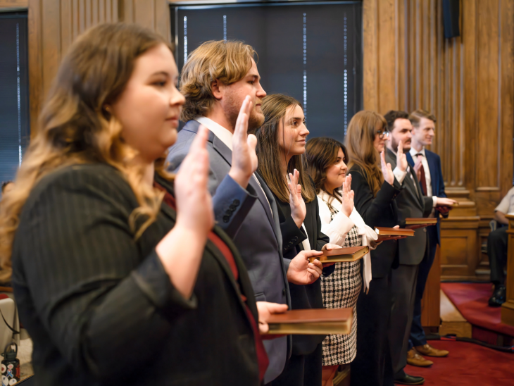 A line of seven people in business attire raising right hands as they take an oath.