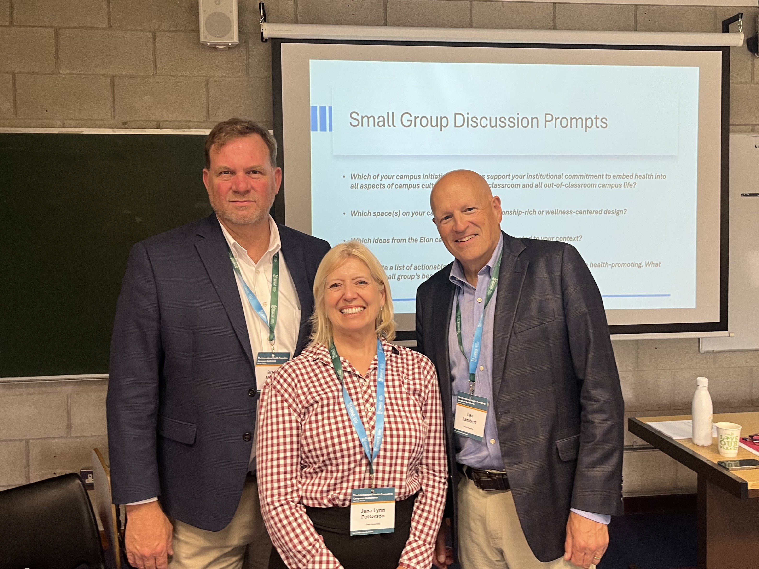 Three people pose for a photo in front a presentation screen