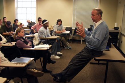 A man in front of a classroom of college students seated at desks.