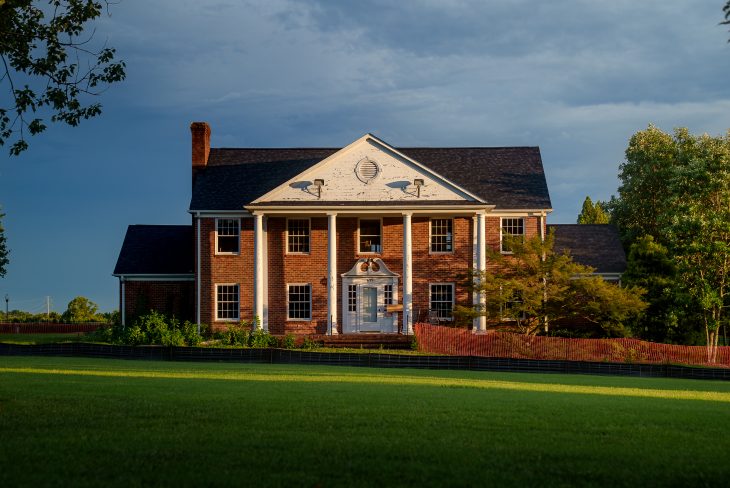 A historic brick building with white columns stands under evening light.