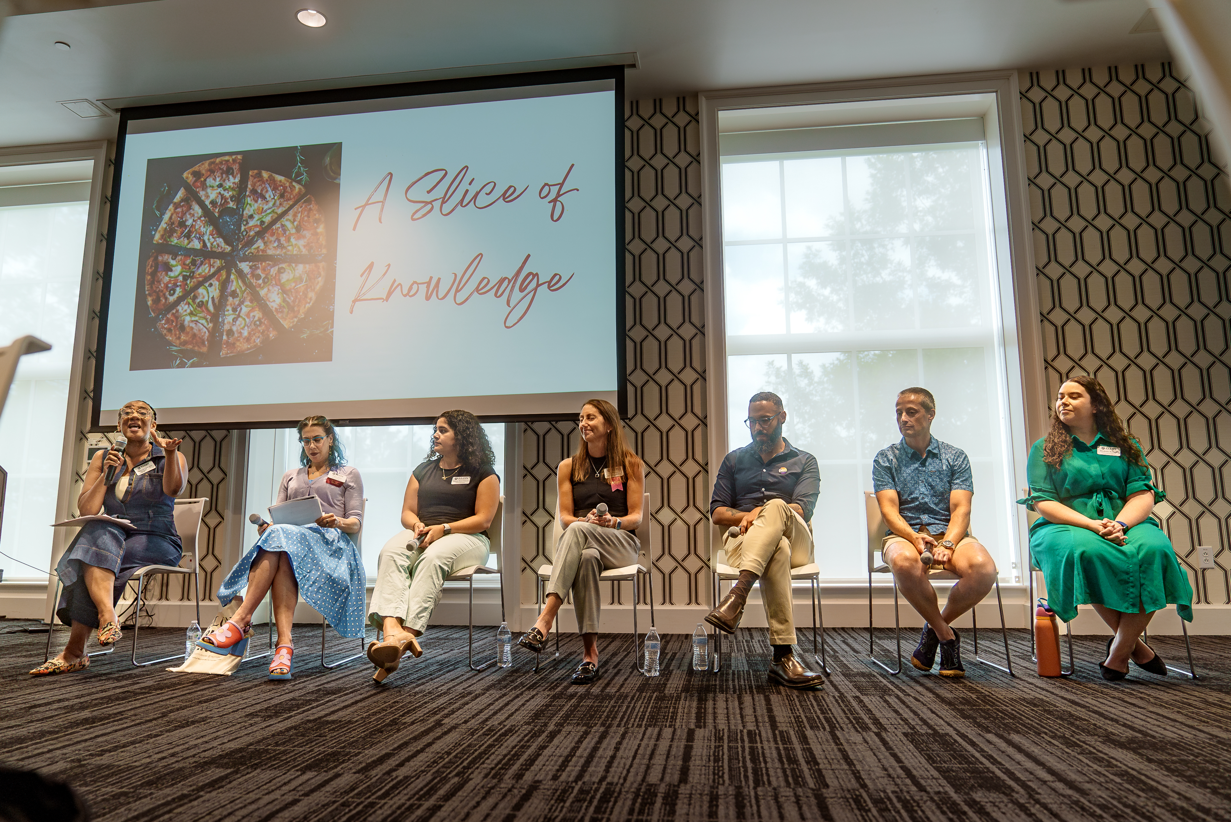 Panelists sit in a row beneath a screen that reads “A Slice of Knowledge” during an Odyssey Week session.