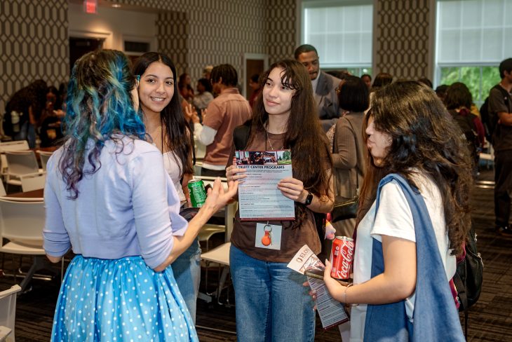 Students engage in conversation and hold program flyers during a networking session at the event.
