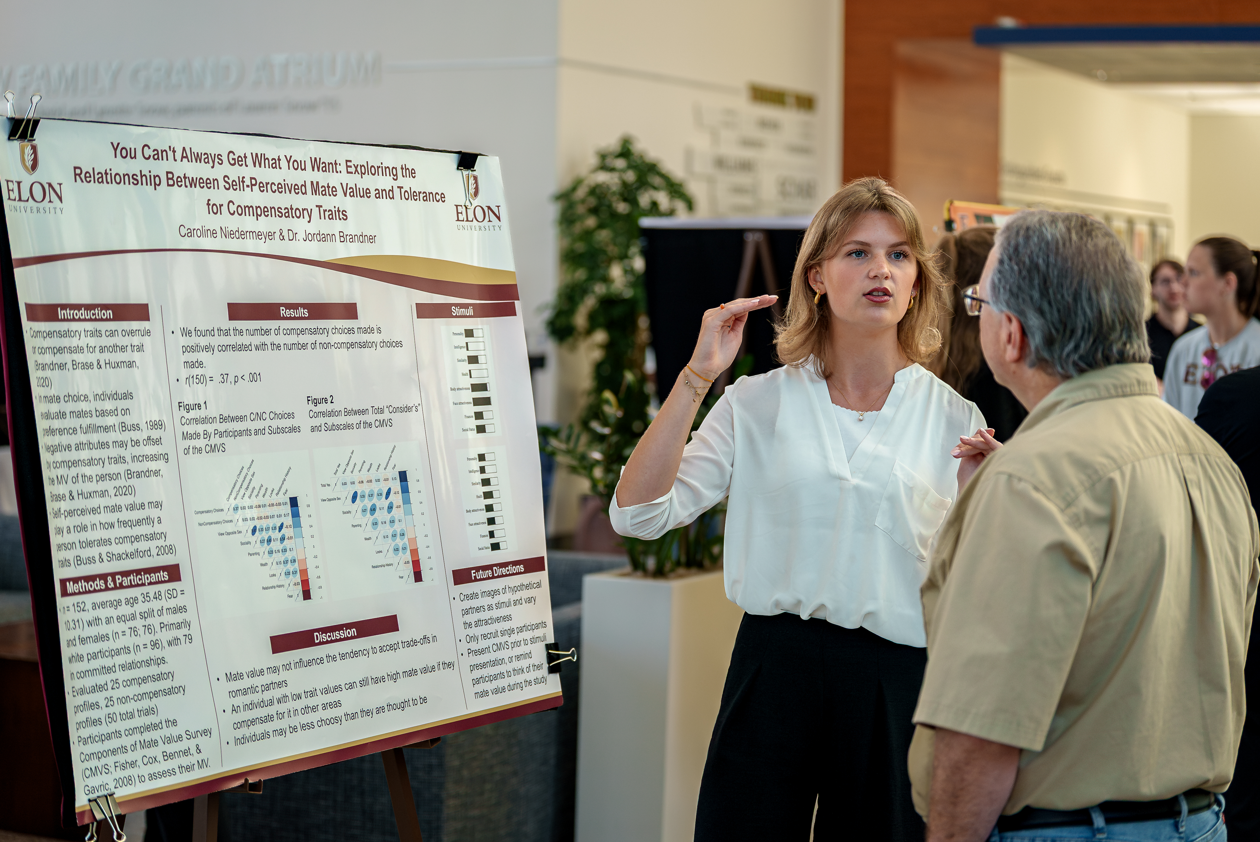 A student discusses her psychology research with a guest, pointing to a poster titled “You Can’t Always Get What You Want.”
