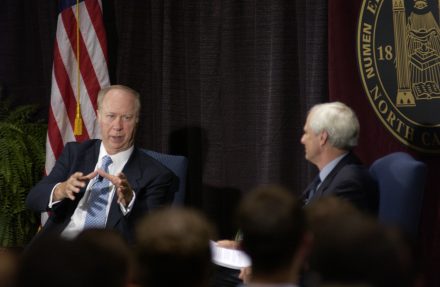 Two men on a stage. An American flat is behind them.