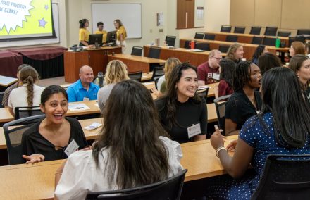A group of students in an amphitheatre style classroom sit facing each other, talking and smiling.