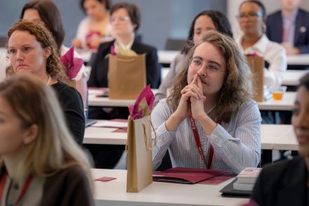 Students seated in a classroom listening intently. There are gift bags and books on the tables next to them.