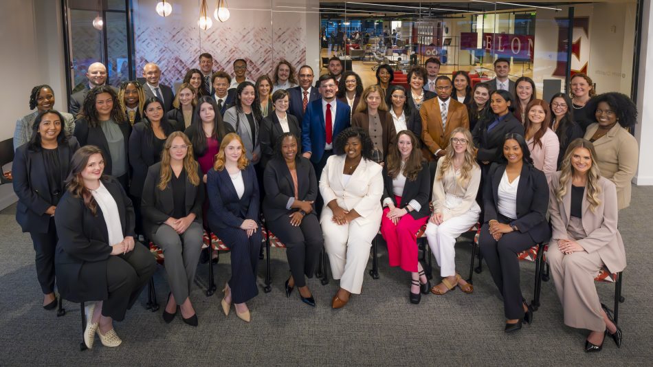 A large group of professionally dressed students pose for a group photo in a glass-walled classroom at Elon University's Charlotte center. The Elon Law Flex Program allows students to attend part-time law school in Charlotte.