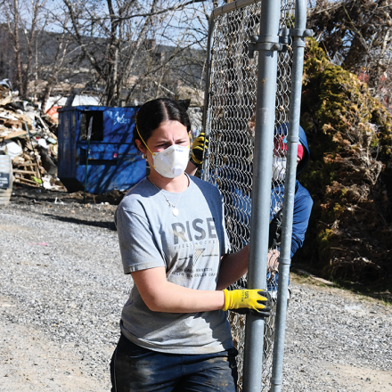 Two volunteers carry a piece of chain link fence.