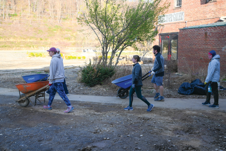 Five volunteers push wheelbarrows down a sidewalk