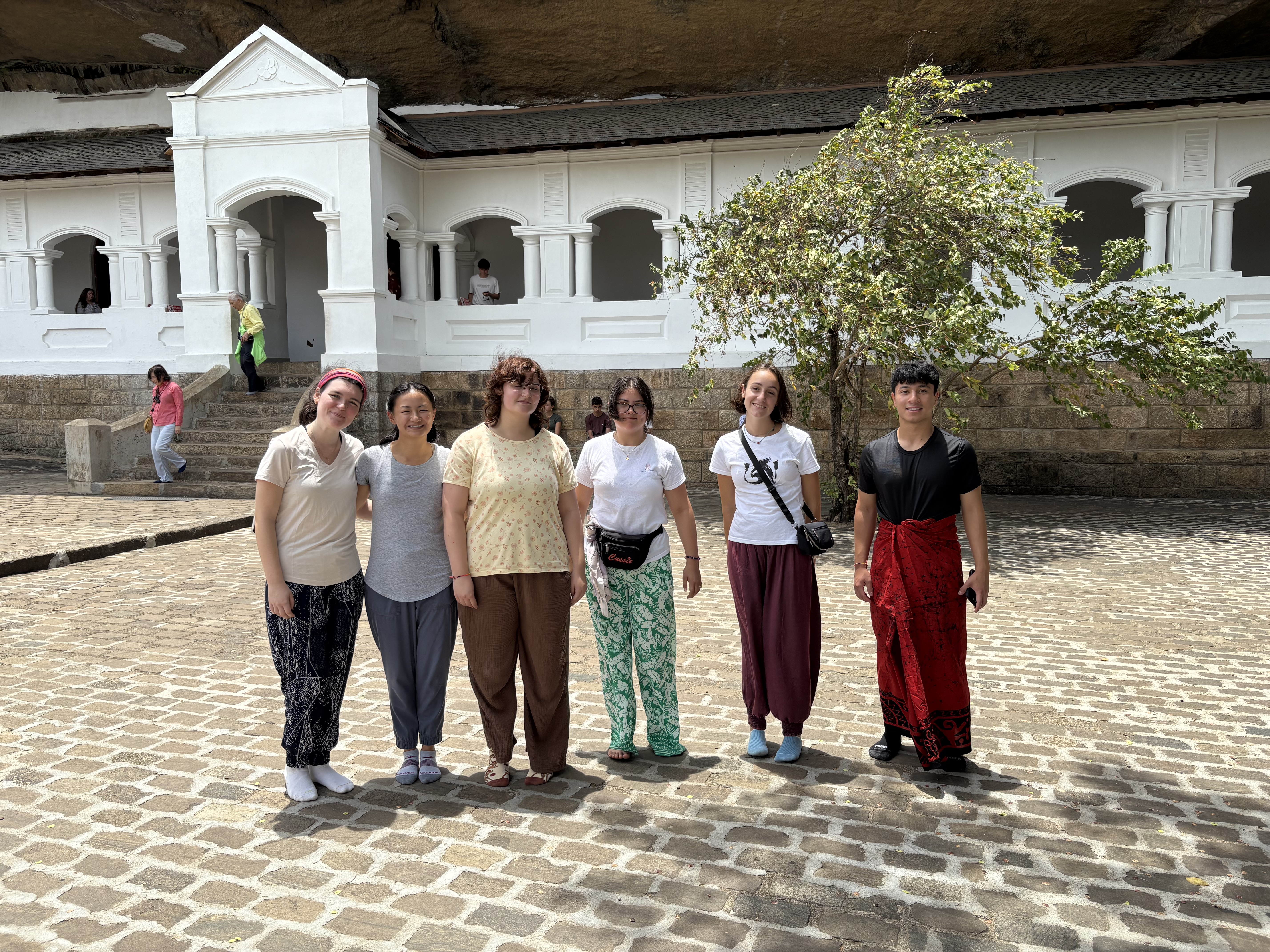 A group of six people pose for a photo on a bricked street