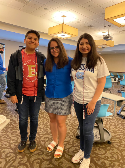 A boy and two girls pose with their arms around each other and smile.
