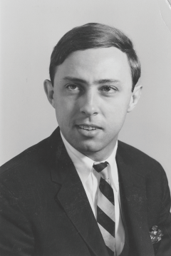 A black and white headshot of a male college student from the 1950s wearing a suit jacket and tie