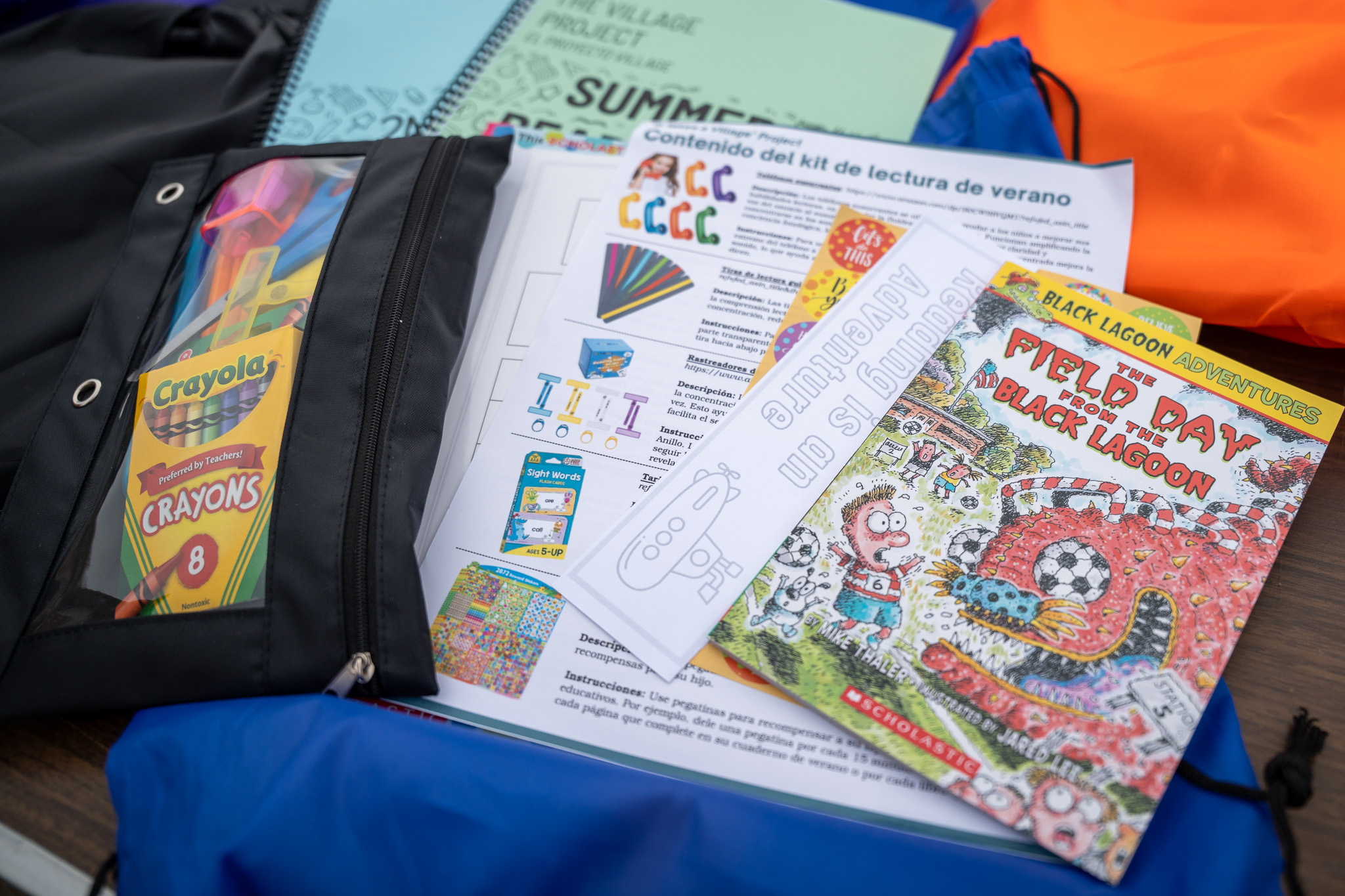 A summer reading kit with crayons, worksheets, a bookmark, and the book “Field Day from the Black Lagoon” is spread out on a table.
