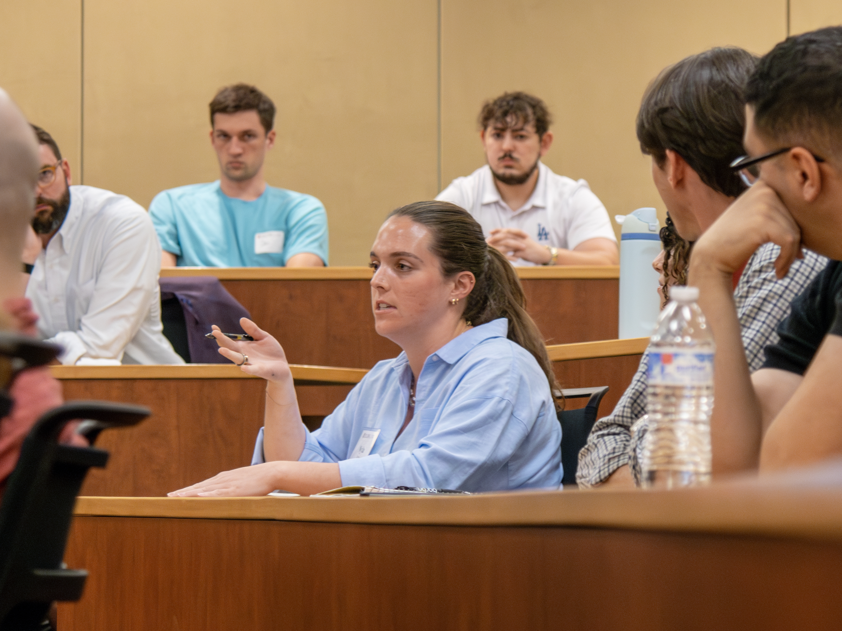 A female student speaking while seated in a classroom. Others around her are listening to what she says.