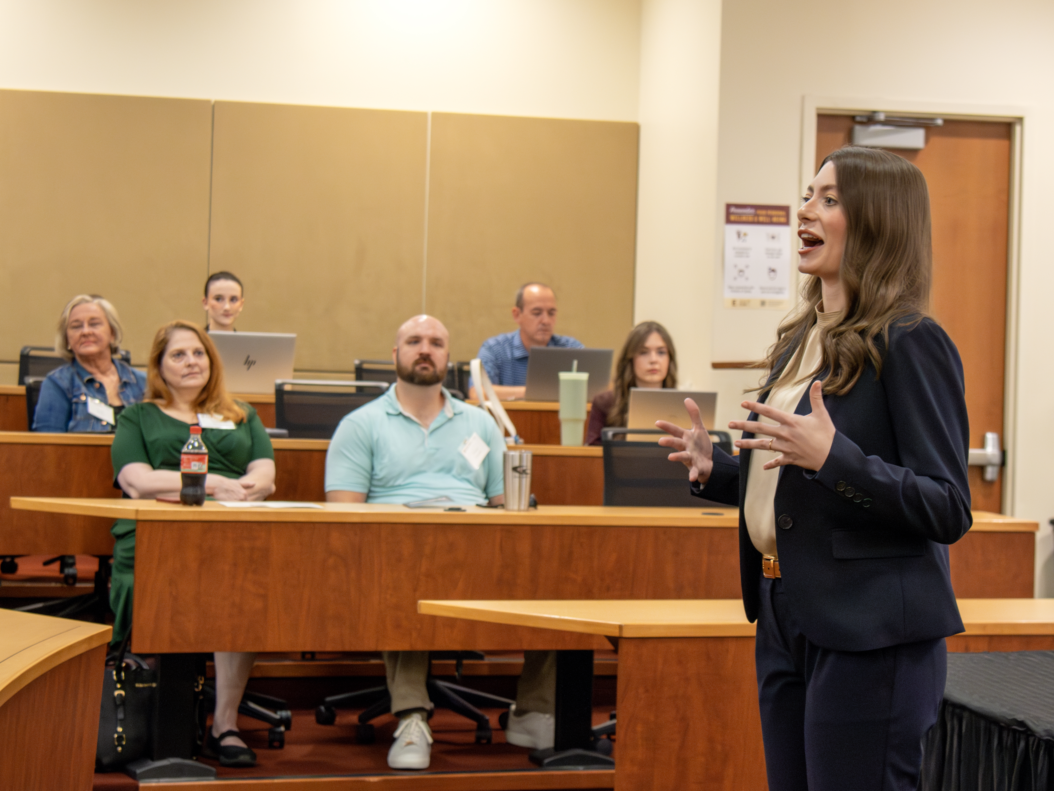 A woman in professional dress speaks to a crowded amphitheatre-style room.