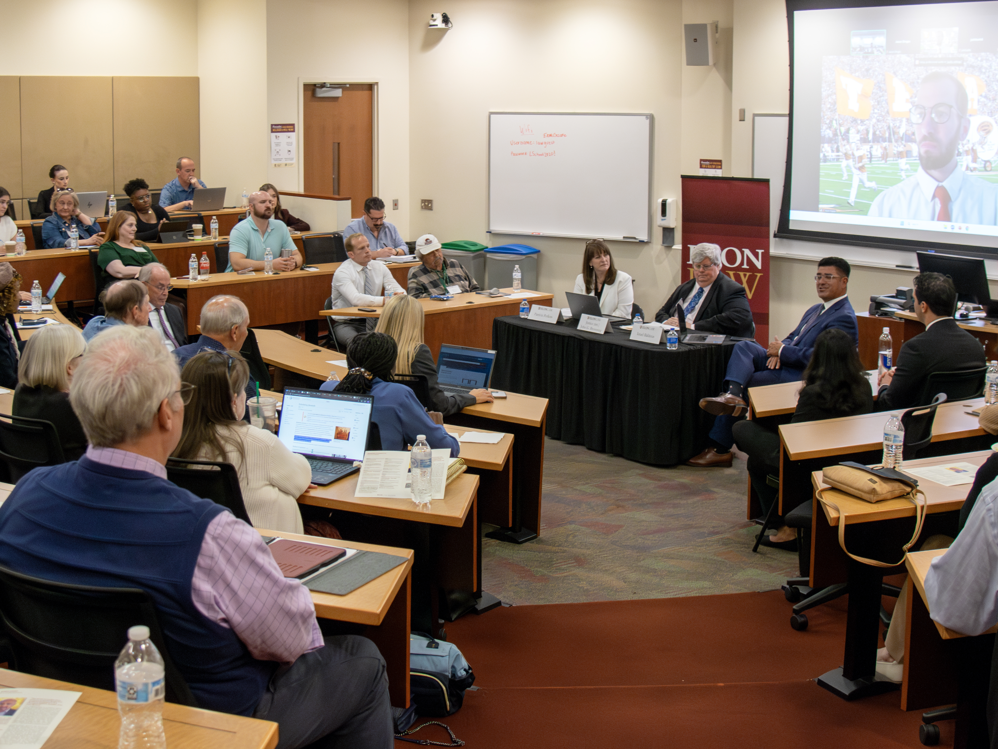 A table with speakers around it at front of a large, crowded amphitheatre-style classroom.