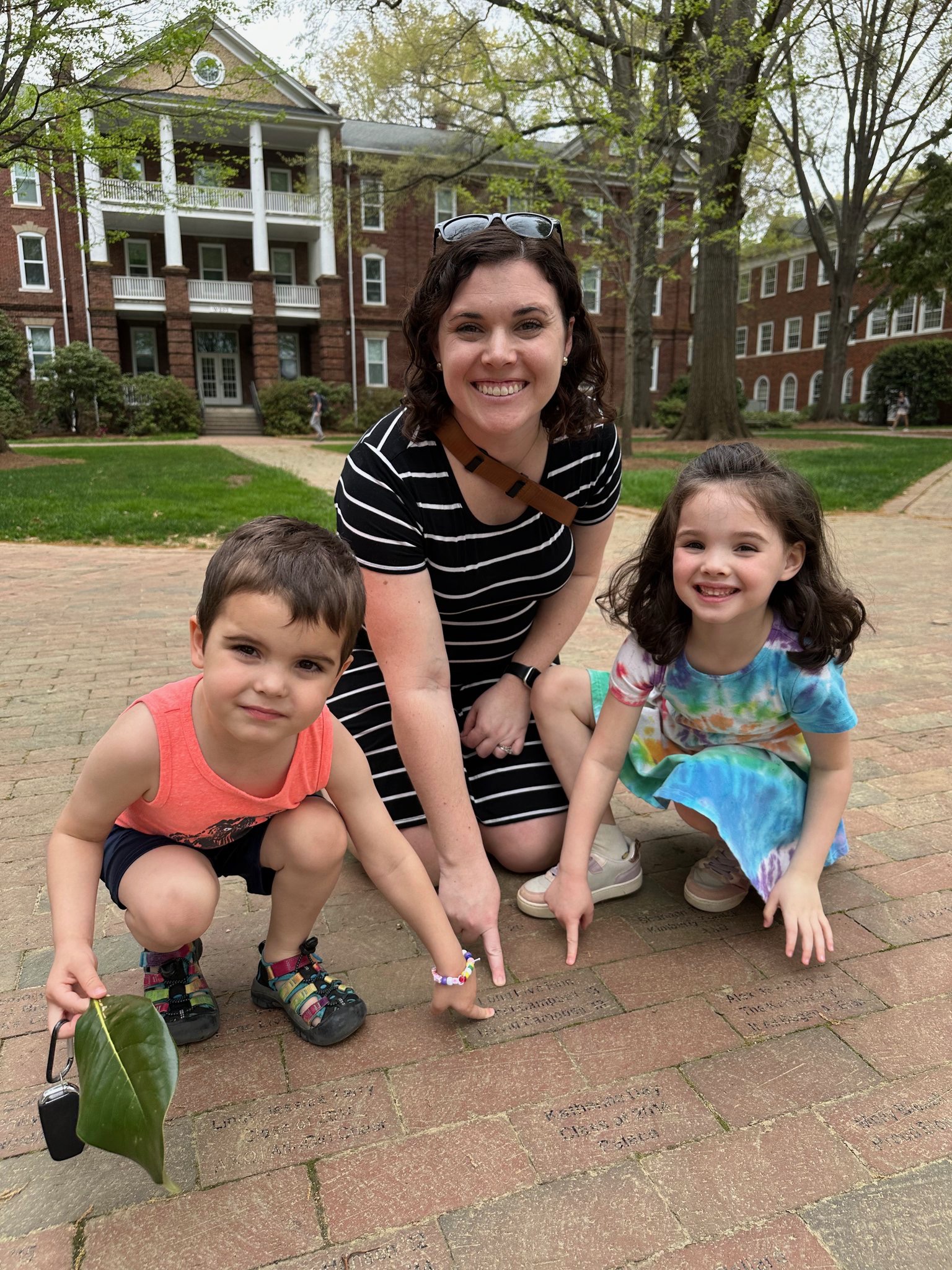 Rachel and 2 of her kids point to her brick at Elon