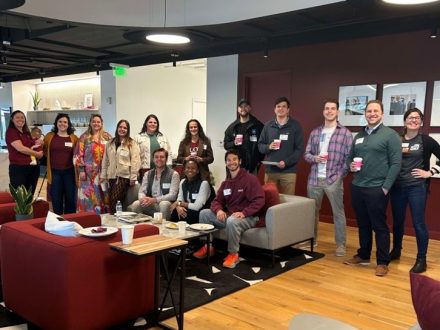 A group of people standing and sitting with drinks and food in hand 