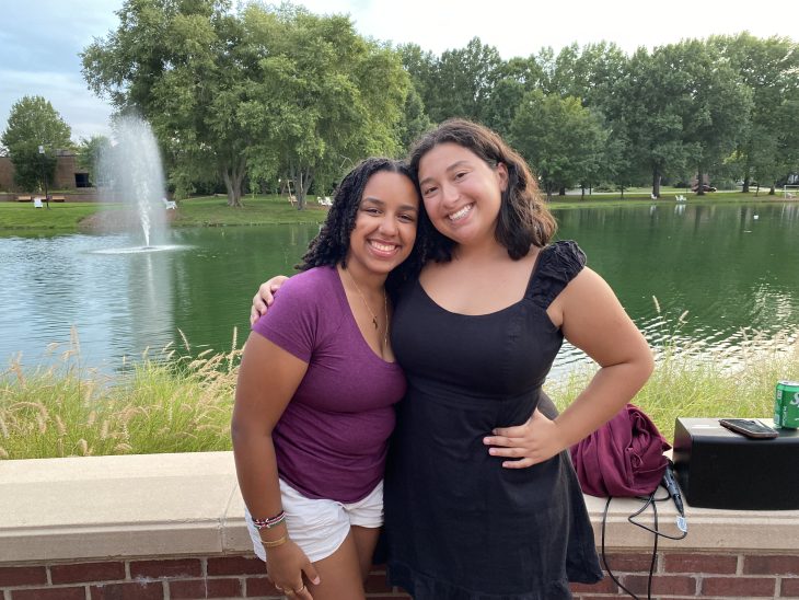 Two students smile in front of Lake Mary Nell with a lush green background.