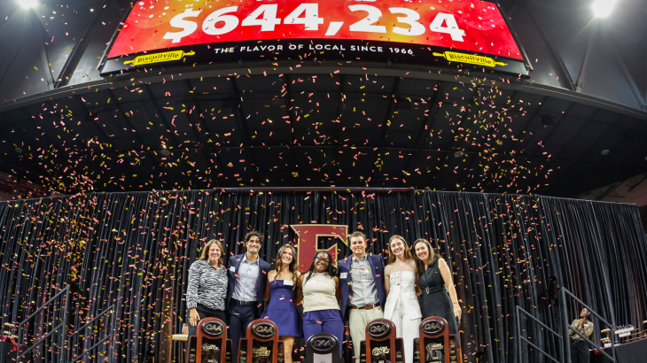 Group of people pose on stage with trophies as confetti falls, celebrating raising $644,234, displayed on the screen above.