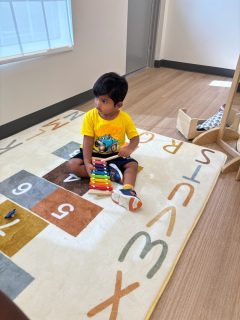 A child wearing a bright yellow shirt plays with a colorful instrument on a light color carpet
