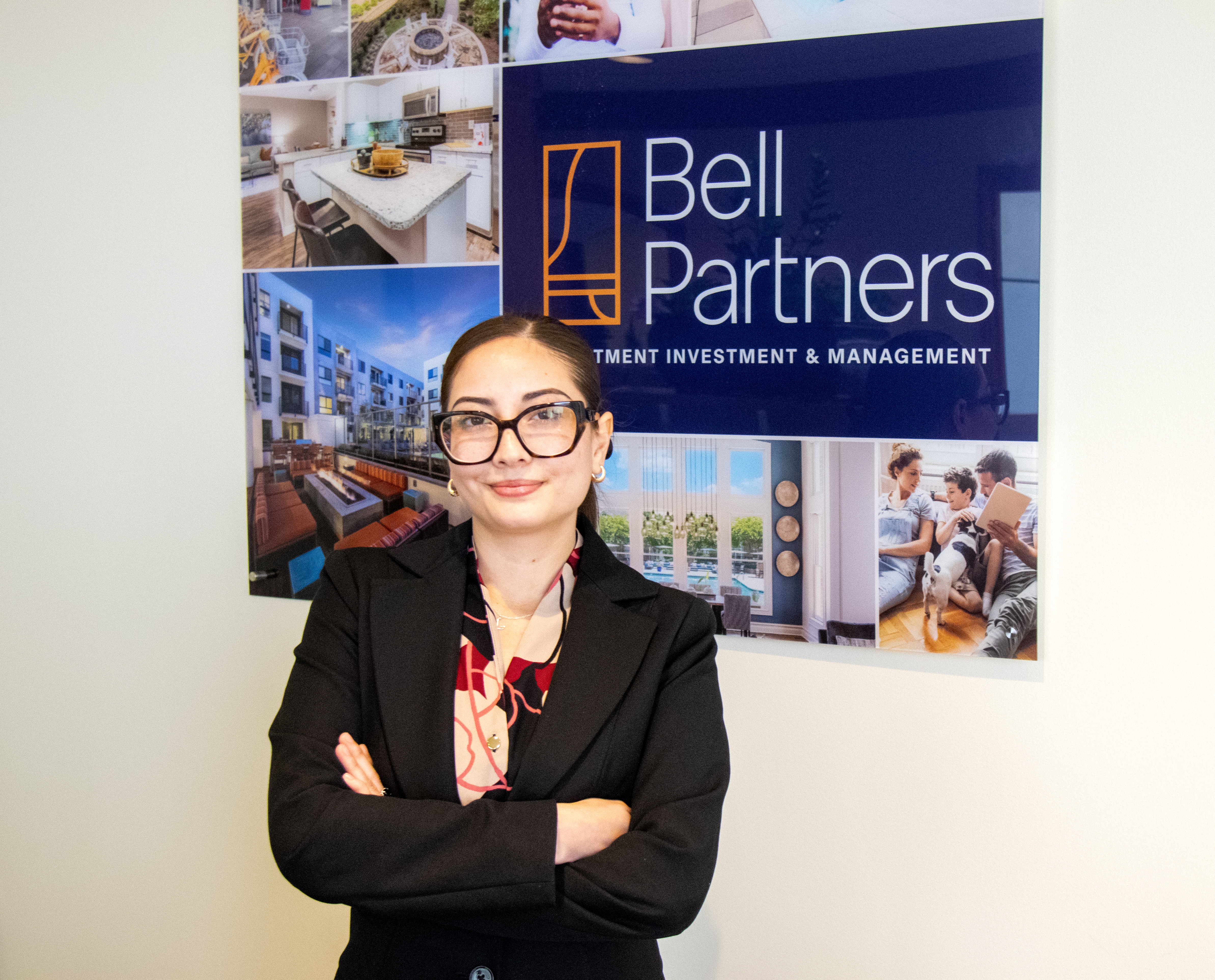 Adriana Hernandez Ordonez in front of the Bell Partners sign. She is smiling with her arms crossed and wearing a business suit.