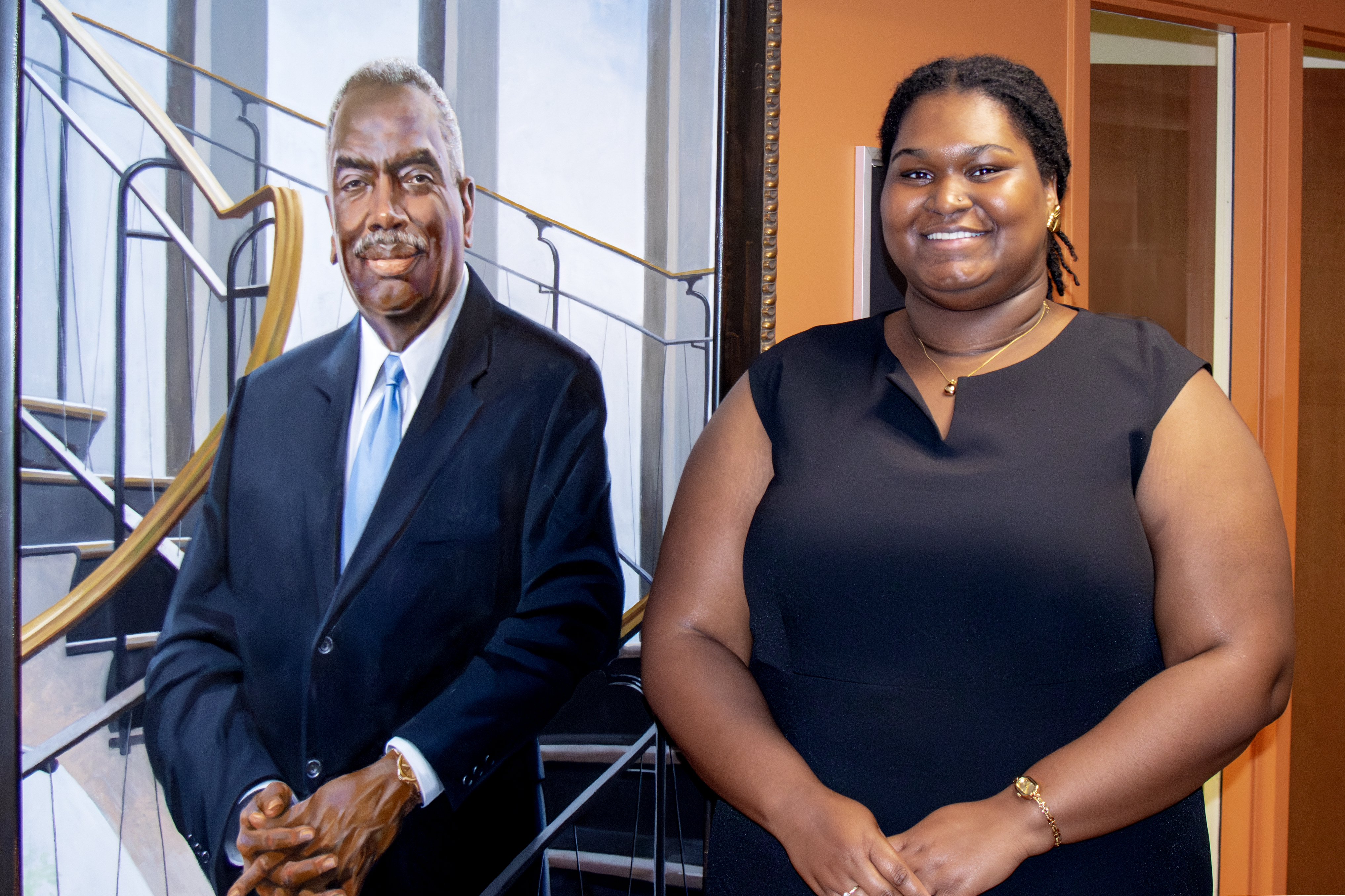 Karrington Wallace in a formal black dress and a painted portrait of Dean Johnson.