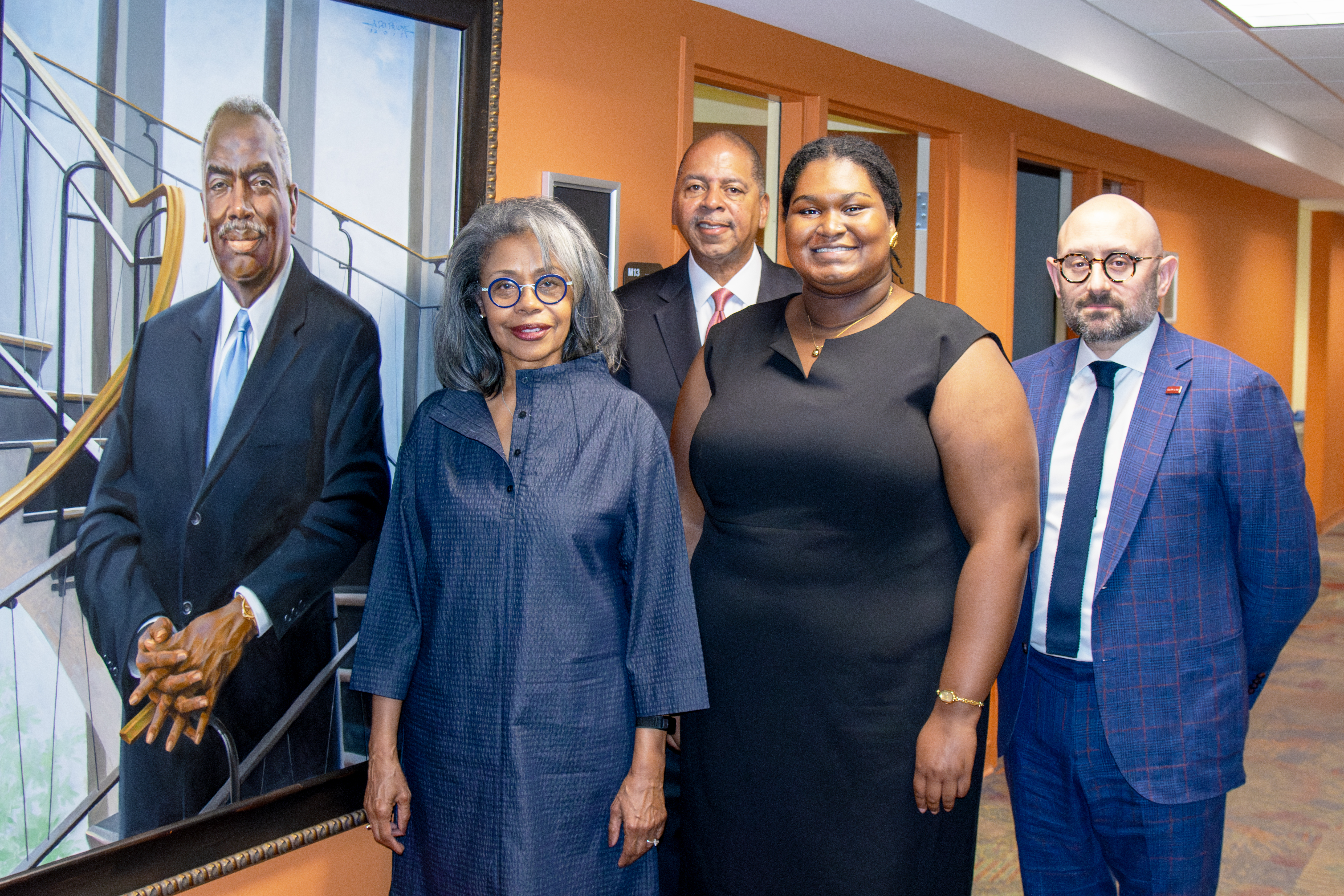 A group of four people in front of a portrait in a library.