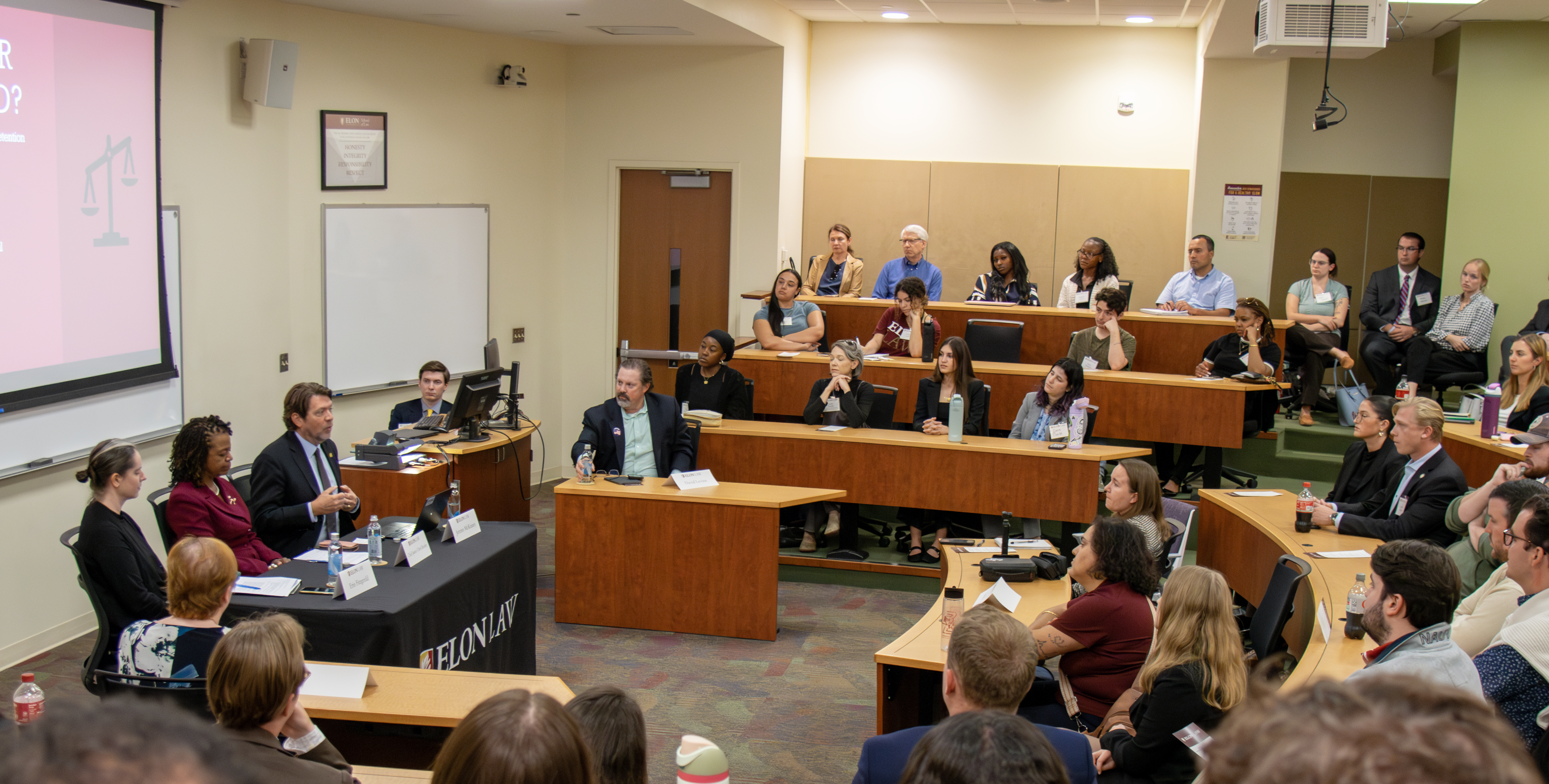 A crowded classroom watches a three-person panel.