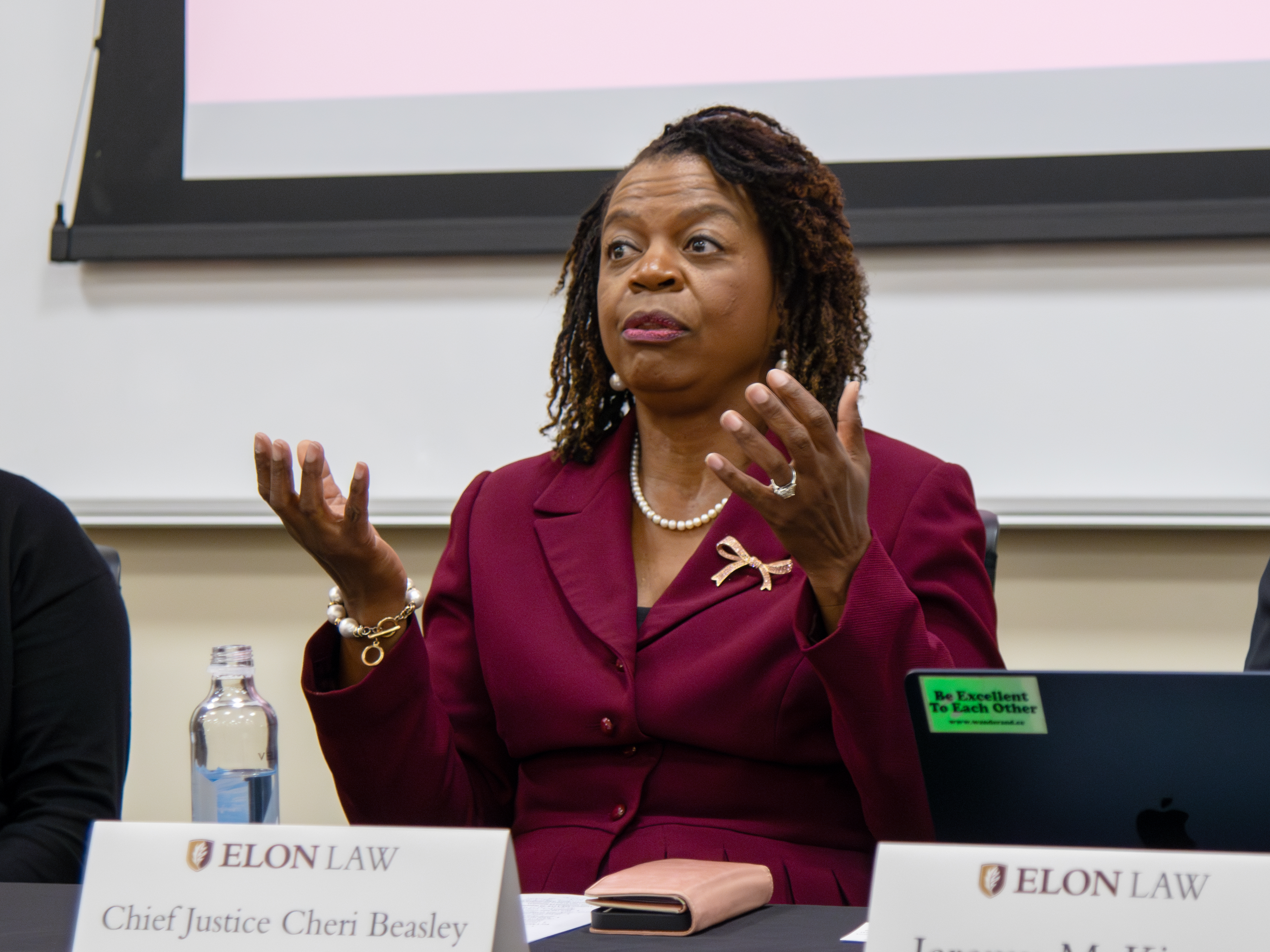 A woman in a maroon business suit gestures while speaking.
