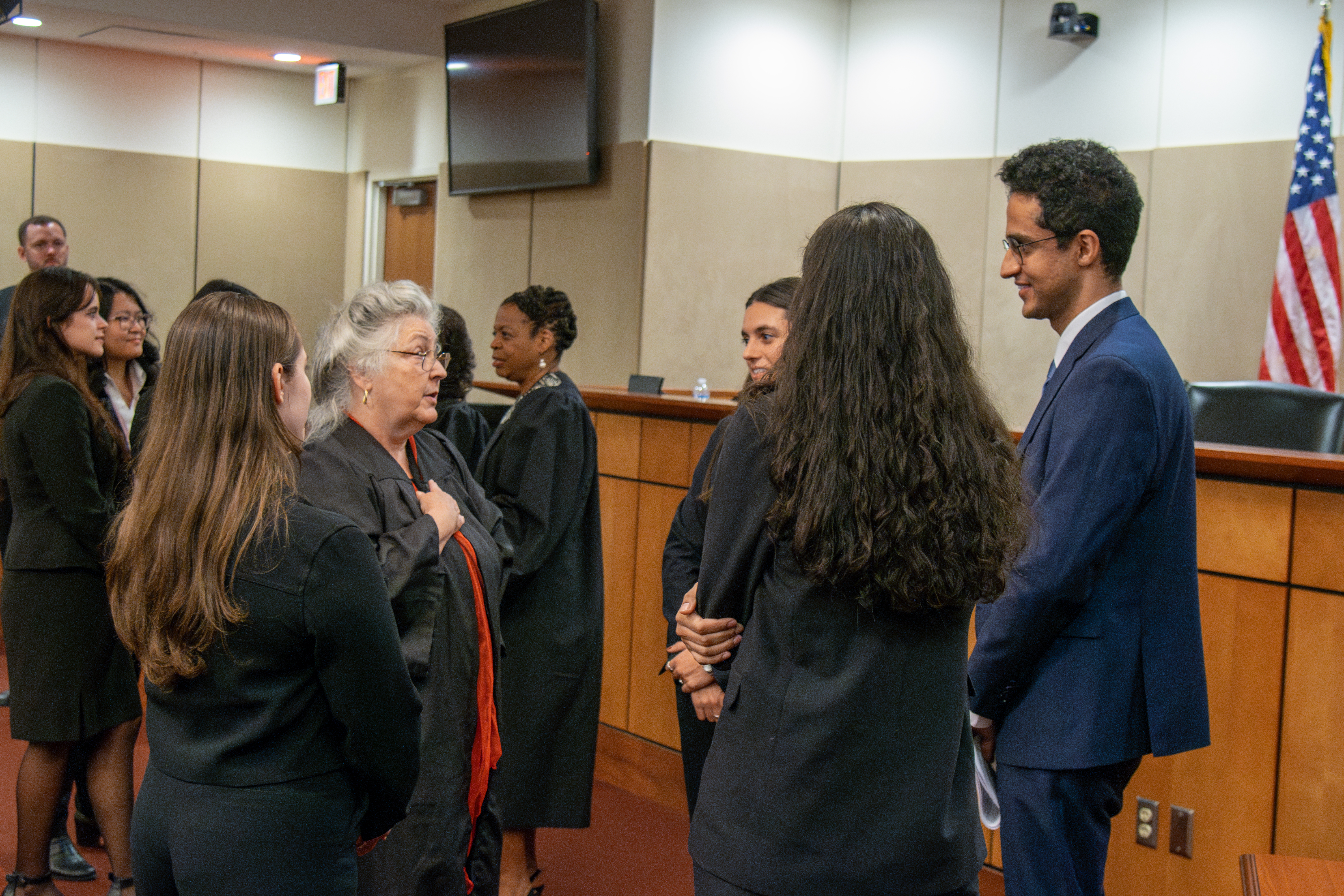 A group of law students circled around a judge during a conversation inside a courtroom.