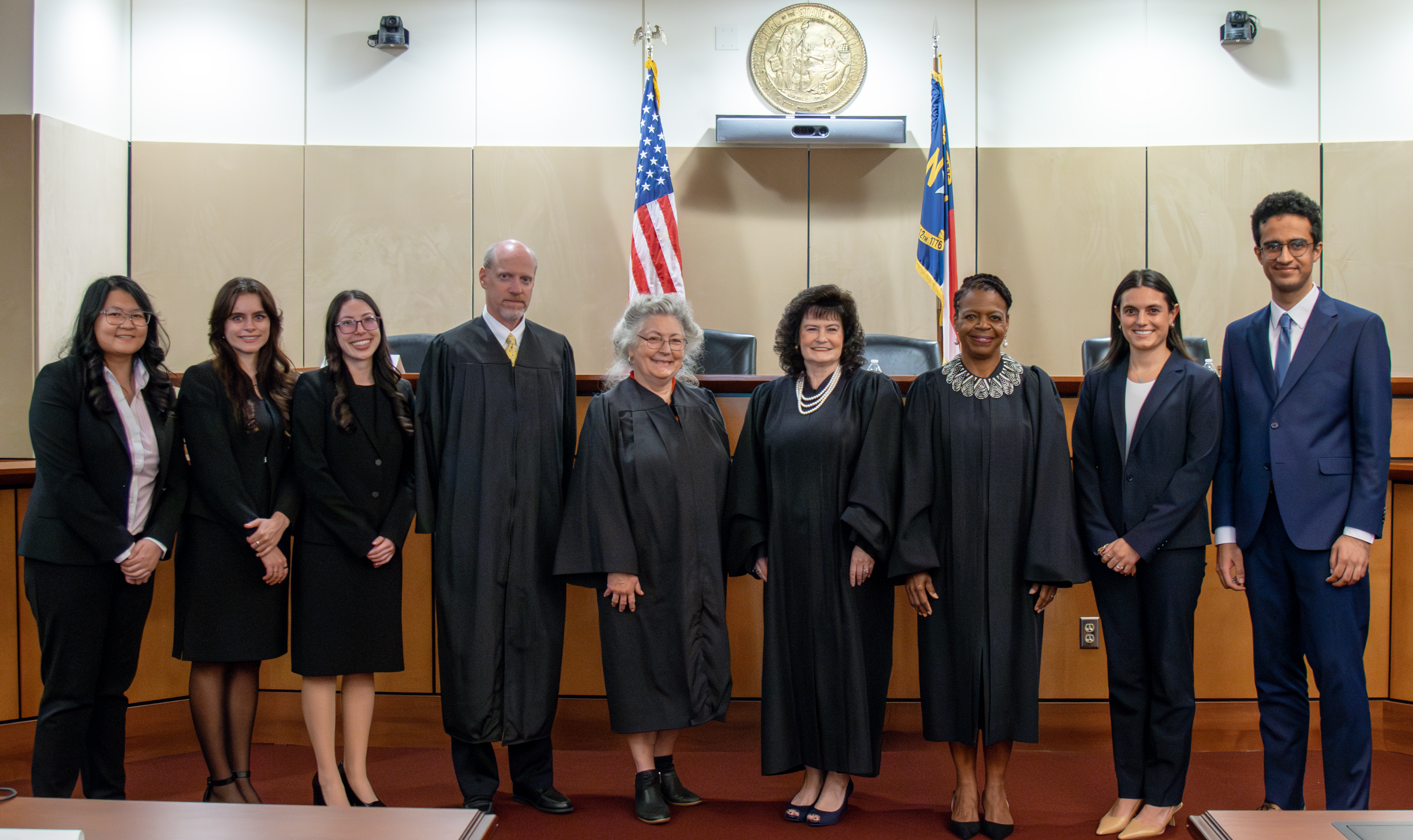 Five law school students flank four judges in the Robert E. Long Courtroom at Elon Law