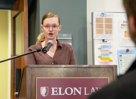 A woman speaks into a microphone at a podium with the Elon Law mark.