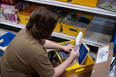 Rosie Fyffe ’27 organizes school supplies into yellow bins while volunteering at Classroom Central. They are sorting notebooks and rulers on a lower shelf surrounded by colorful containers and boxes.
